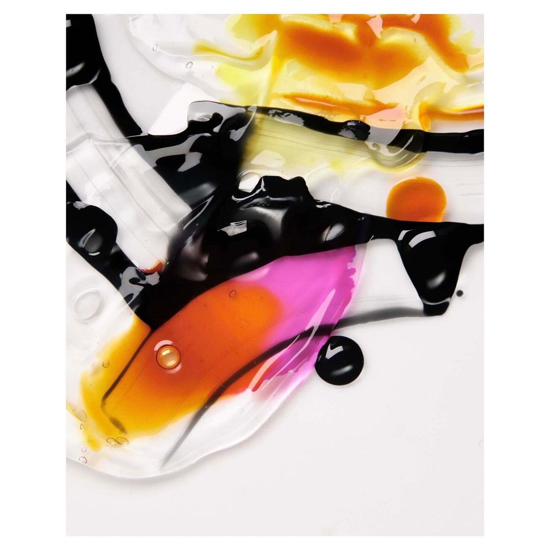 Abstract close-up of beauty product smears in pink, yellow, and black on a white background, showing texture and color variations.
