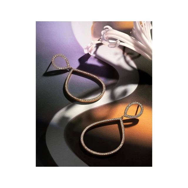 Elegant teardrop earrings with shimmering accents on a patterned surface, complemented by a delicate white flower, creating a soft, luxurious aesthetic.