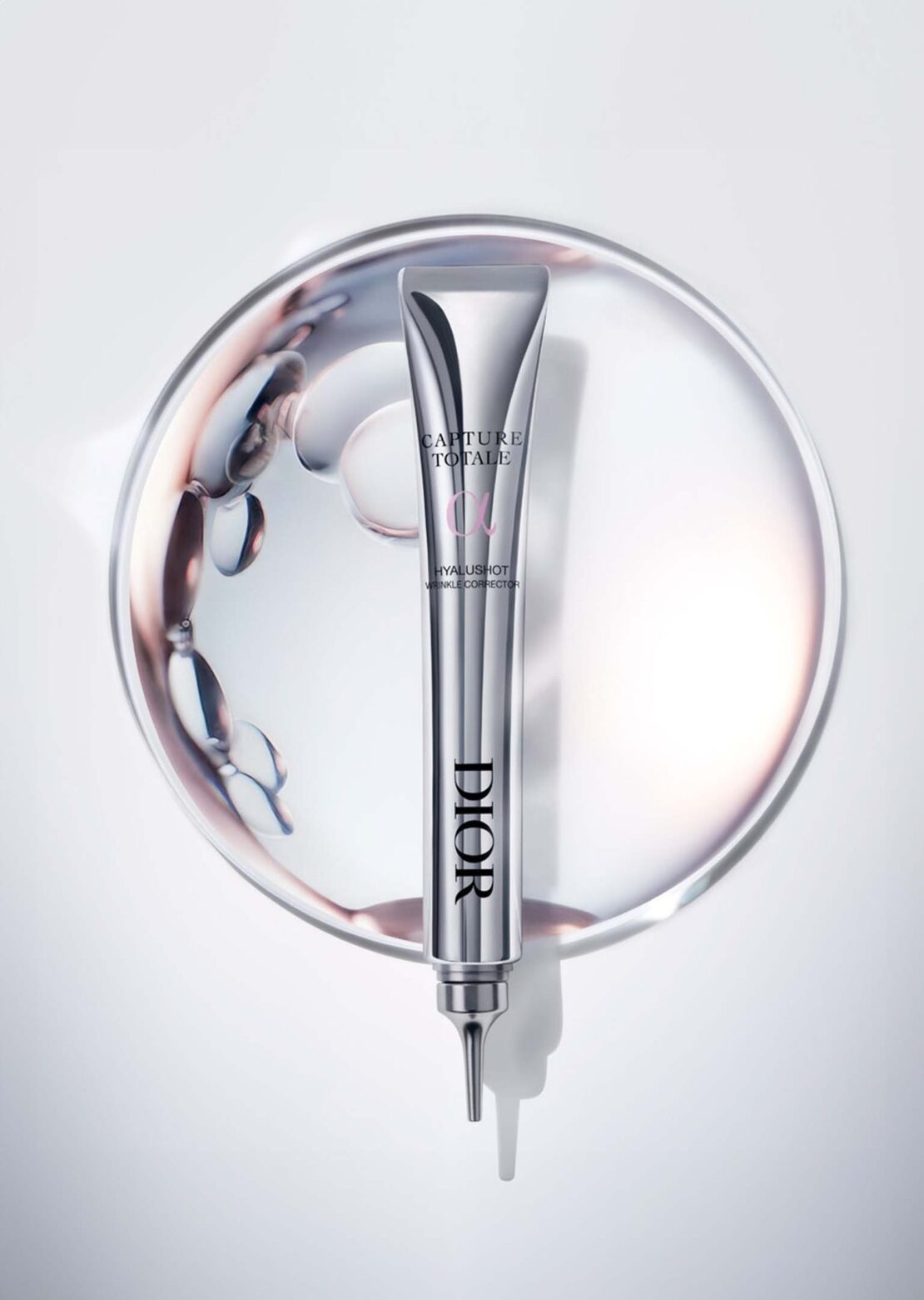 Elevated view of a Dior Capture Totale Hyalushot tube on a silver plate with swirling liquid, captured in a studio setting, showcasing beauty product.