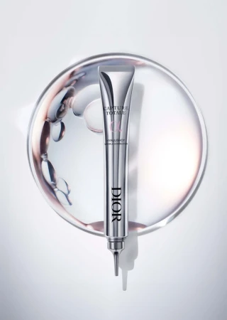 Elevated view of a Dior Capture Totale Hyalushot tube on a silver plate with swirling liquid, captured in a studio setting, showcasing beauty product.