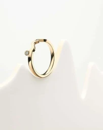 Minimalist gold ring with a single embedded diamond resting on a sculpted white textured background