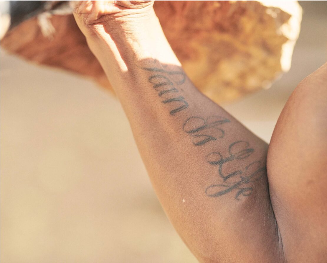 Close-up shot of adult human arm with a tattoo that says 'Pain is Life,' captured in soft, diffused lighting conditions outdoors.
