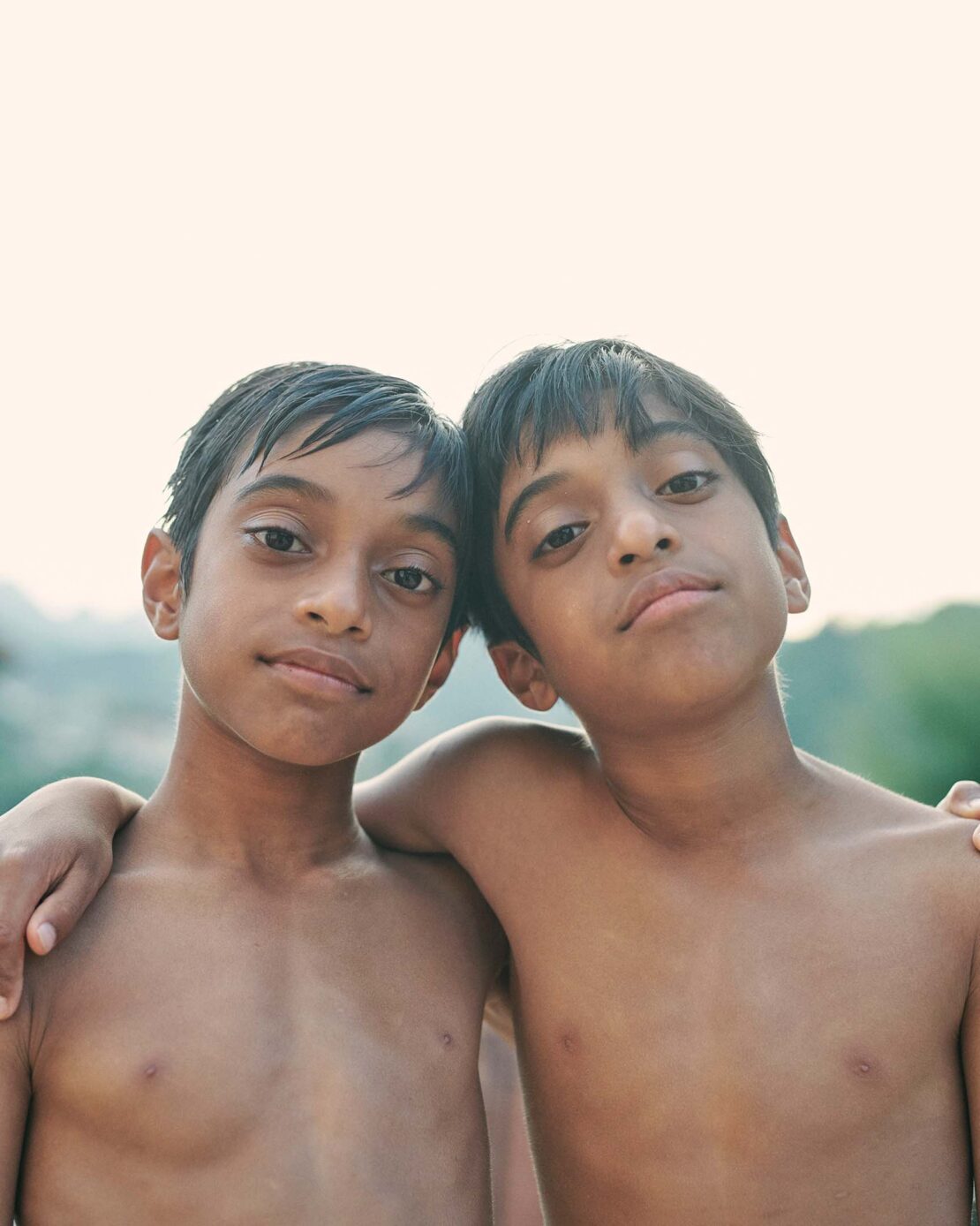 Portrait of two young boys standing closely together with arms around each other against an outdoor light background