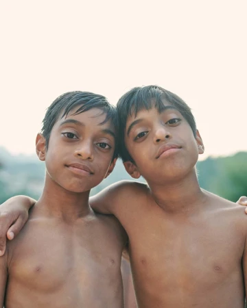 Portrait of two young boys standing closely together with arms around each other against an outdoor light background