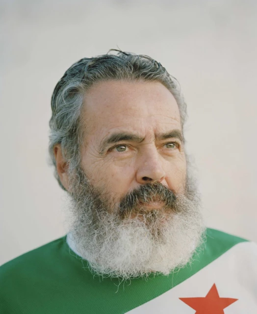 Portrait of a mature adult male with salt and pepper hair and full white beard, wearing a green, white, and red star athletic shirt.