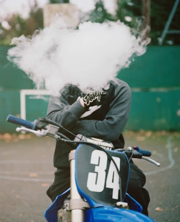 Person obscured by a thick cloud of white smoke seated on a blue dirt bike with number 34 visible on the front.