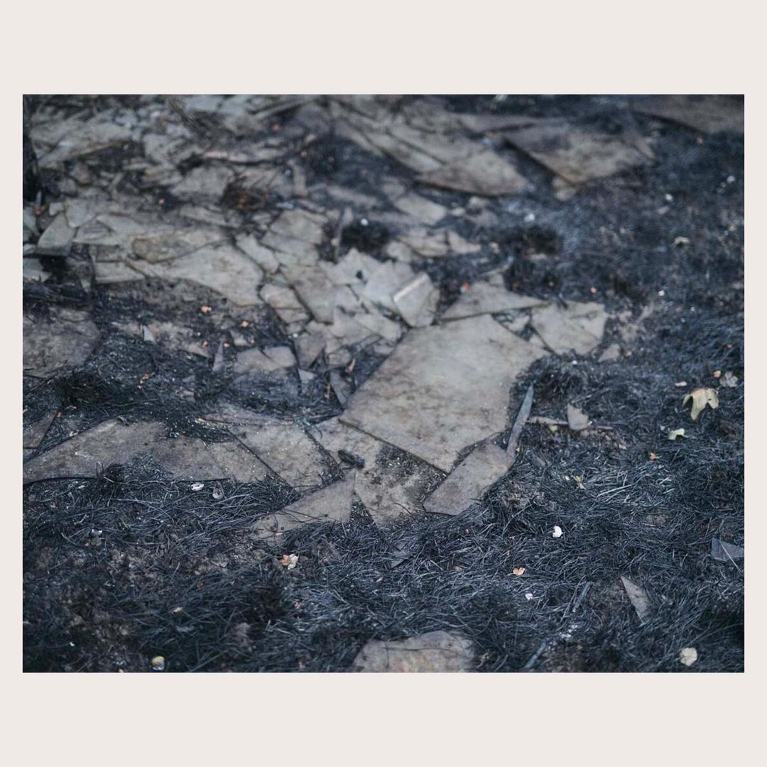 Broken glass shards on a dark, grassy surface create an abstract, textured composition with dominant gray and black hues.