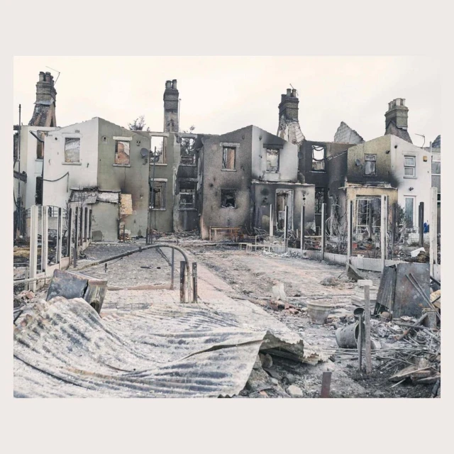 Destroyed row of houses with visible damage and debris in the aftermath of a fire, with chimneys still standing.