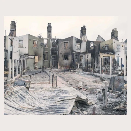Destroyed row of houses with visible damage and debris in the aftermath of a fire, with chimneys still standing.
