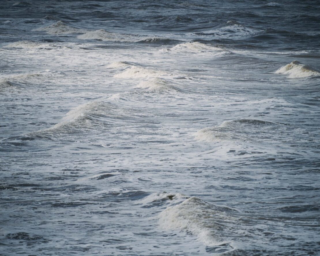 View of ocean water showing waves with white foam tops on a cloudy day with grey-blue color, outdoor environment, nature photography.
