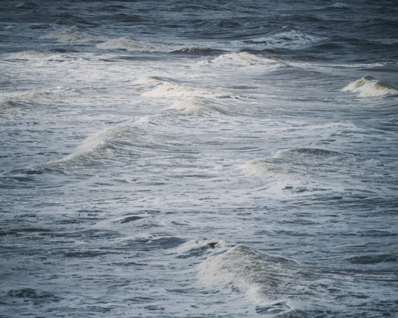 View of ocean water showing waves with white foam tops on a cloudy day with grey-blue color, outdoor environment, nature photography.