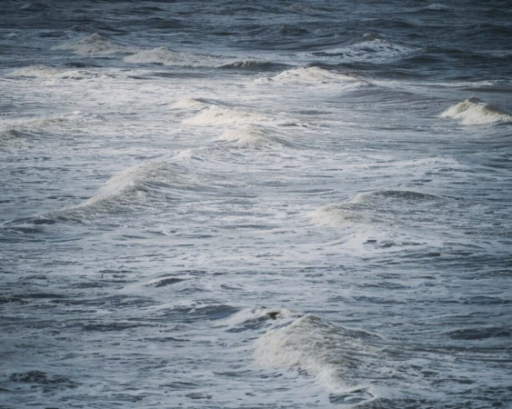 View of ocean water showing waves with white foam tops on a cloudy day with grey-blue color, outdoor environment, nature photography.
