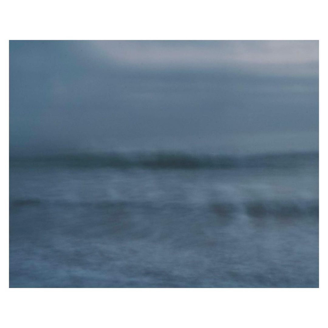 Atmospheric ocean view featuring blurred waves and a cloudy sky, conveying a sense of calm and motion in a monochromatic palette.