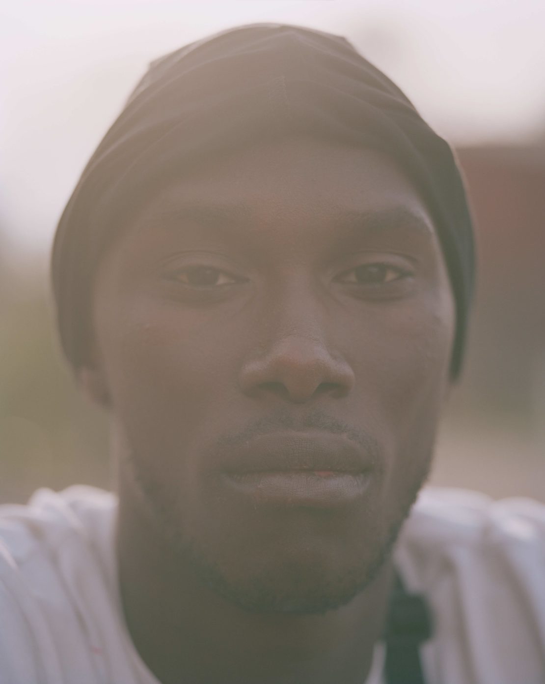 Close-up studio portrait of an adult Black man wearing a black cap, looking directly at the camera with a neutral expression.