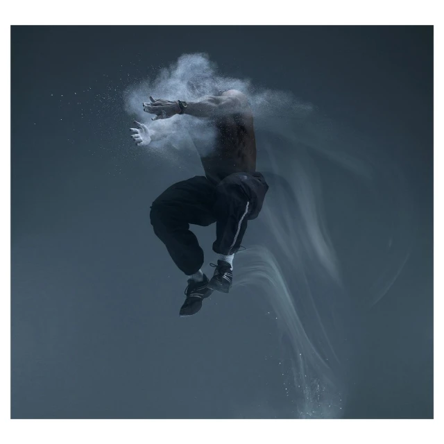 A muscular man mid-air, seemingly suspended in a cloud of white powder against a dark grey background, creating a dynamic, artistic composition.