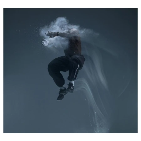 A muscular man mid-air, seemingly suspended in a cloud of white powder against a dark grey background, creating a dynamic, artistic composition.