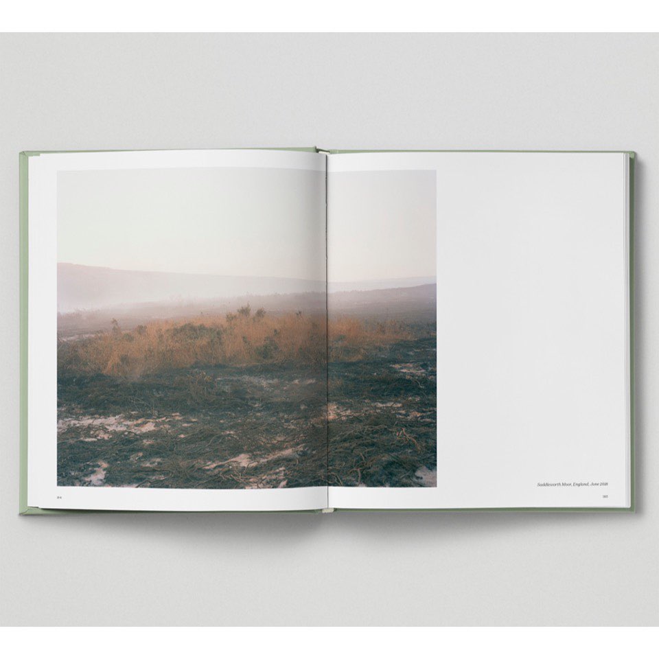 Open book displaying a landscape photograph of a misty, grassy field with hills in the background, on a white surface.