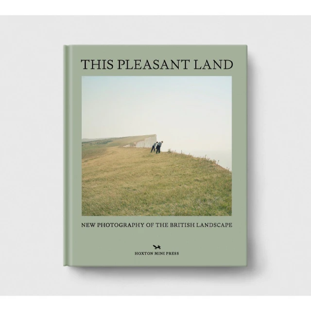 Book cover with photograph of two people on a grassy cliff overlooking the sea, titled 'This Pleasant Land' by Hoxton Mini Press.
