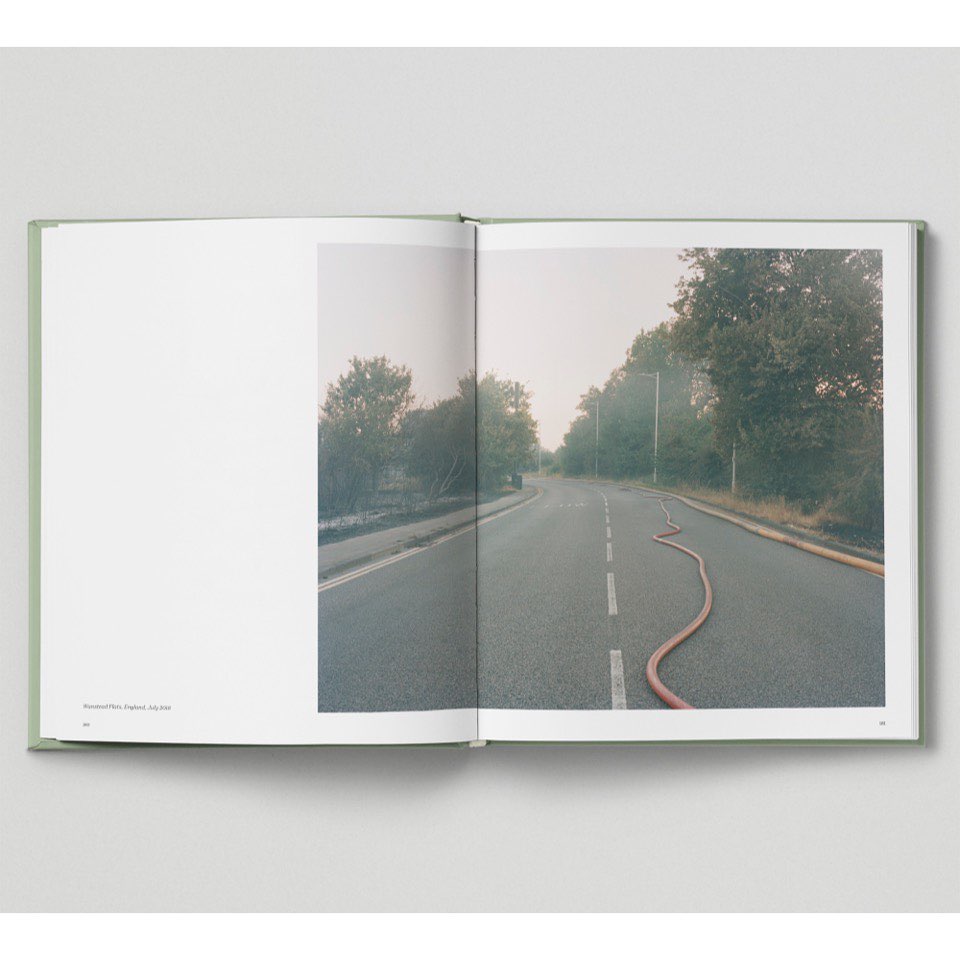 Photograph of a road with a fire hose running along the center median, flanked by trees, as seen in an open book against a white backdrop.