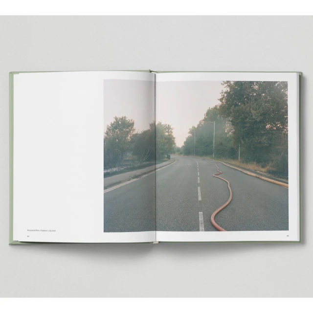 Photograph of a road with a fire hose running along the center median, flanked by trees, as seen in an open book against a white backdrop.