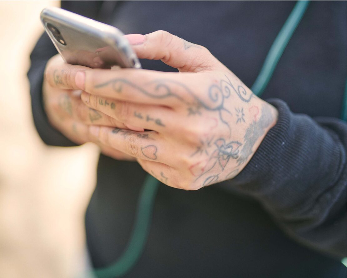 Close-up of tattooed hands holding and using a smartphone while wearing a dark long-sleeve top.