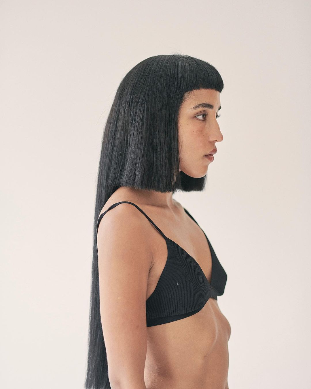 Portrait of a slender adult female in a black bra with a blunt bob haircut against a light backdrop. Beauty, fashion, and hair concept.