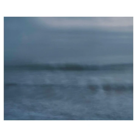 Impressionistic long exposure photograph of ocean waves breaking on a misty shoreline under an overcast sky.