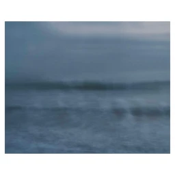 Impressionistic long exposure photograph of ocean waves breaking on a misty shoreline under an overcast sky.