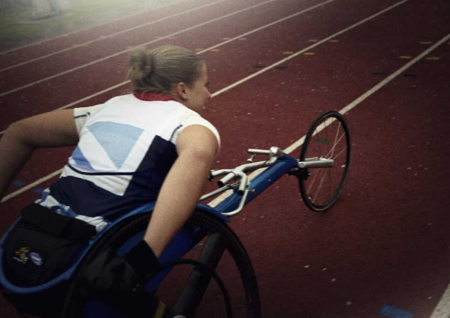 Female athlete competing in a track race using a wheelchair, showcasing speed and determination on a red running track.