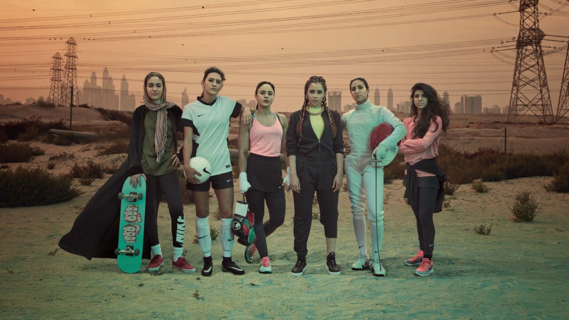 Group of six diverse female athletes stand outdoors in athletic wear against an urban skyline and power lines in a sports lifestyle shot.