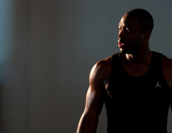 Black man wearing a black athletic tank top looking sideways against a dark studio background