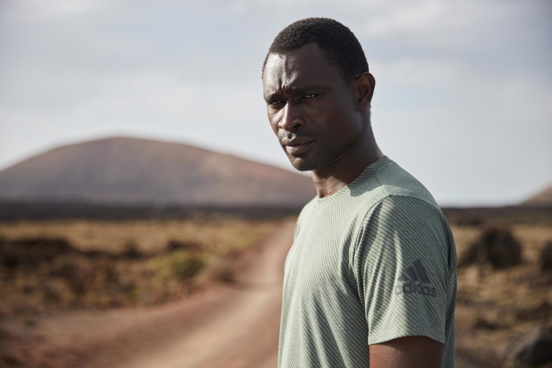Portrait of an adult male in an activewear t-shirt in a desert environment with a dirt road leading to a distant mountain.