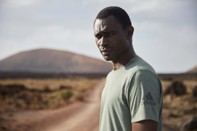 Portrait of an adult male in an activewear t-shirt in a desert environment with a dirt road leading to a distant mountain.