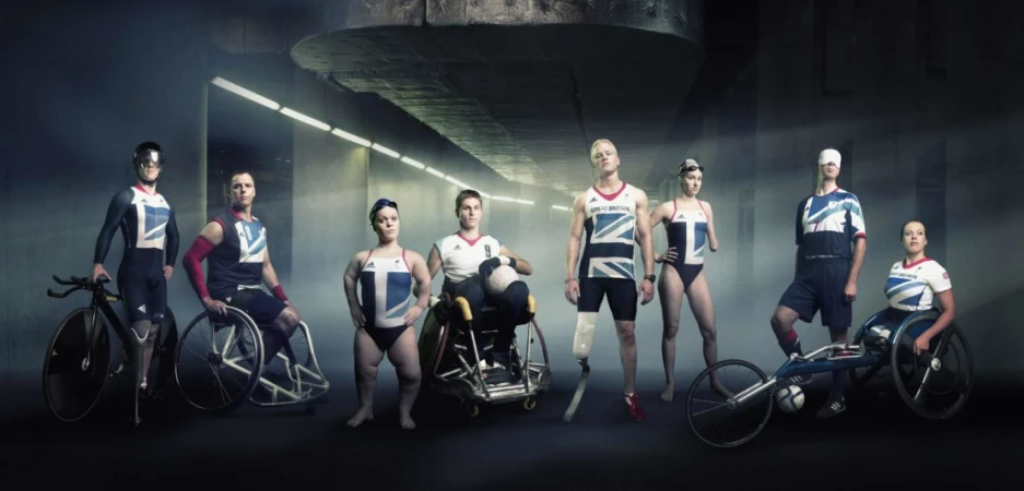 Group portrait of diverse athletes with disabilities in Great Britain sports uniforms in a concrete tunnel with soft, diffused lighting.