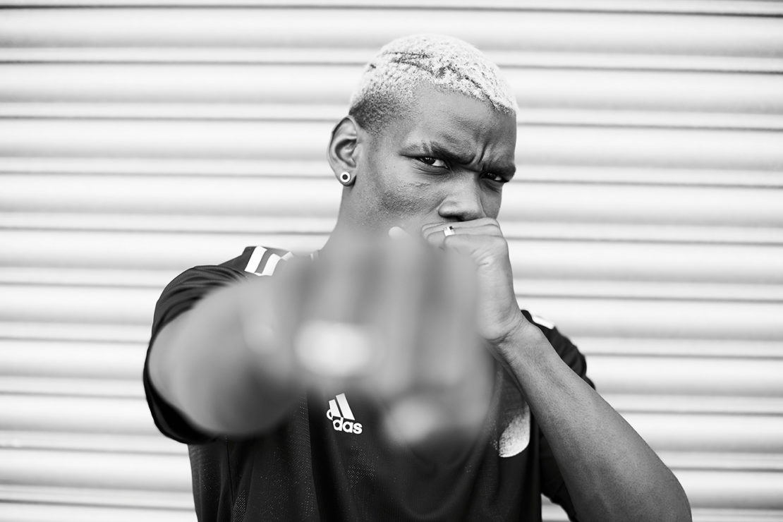 Monochrome close-up of a man in a sports jersey with a determined expression, fist clenched, set against a grey, corrugated metal background.