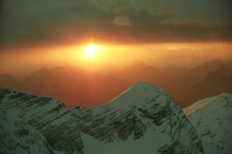 Scenic view of snow-capped mountains with the sun glowing brightly in the sky, creating a warm and ethereal atmosphere.
