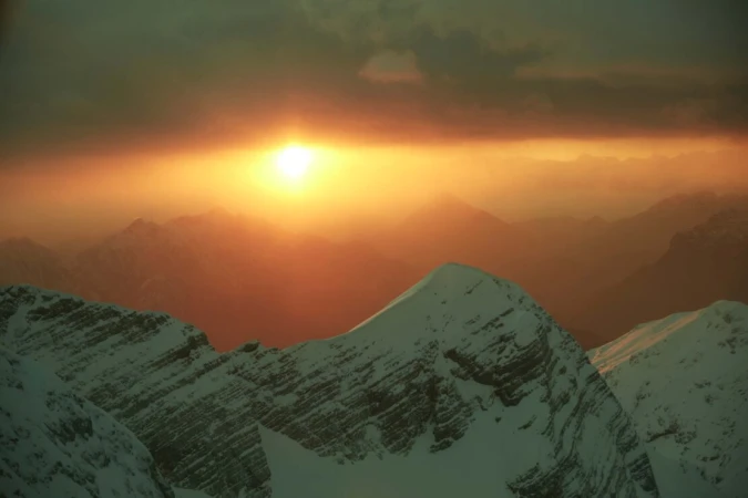 Scenic view of snow-capped mountains with the sun glowing brightly in the sky, creating a warm and ethereal atmosphere.