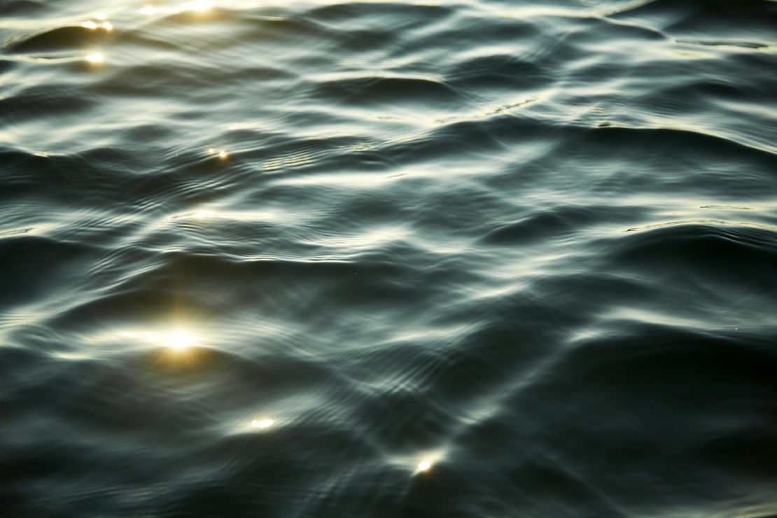 Close-up view of dark water ripples with bright sunlight glinting across the gentle undulating surface.