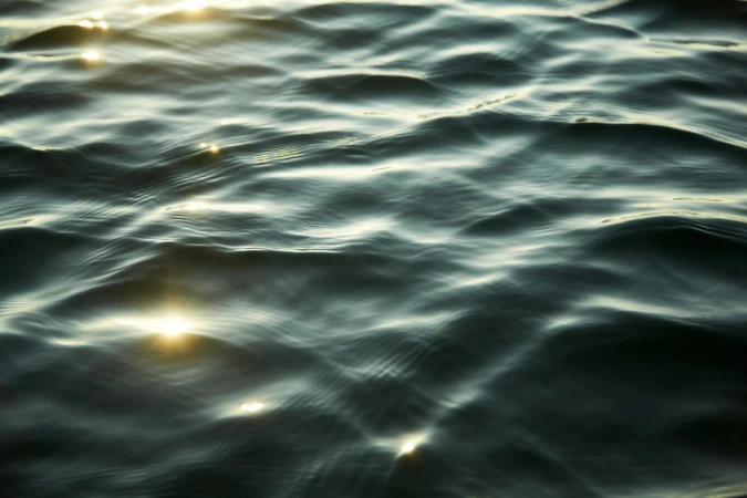 Close-up view of dark water ripples with bright sunlight glinting across the gentle undulating surface.