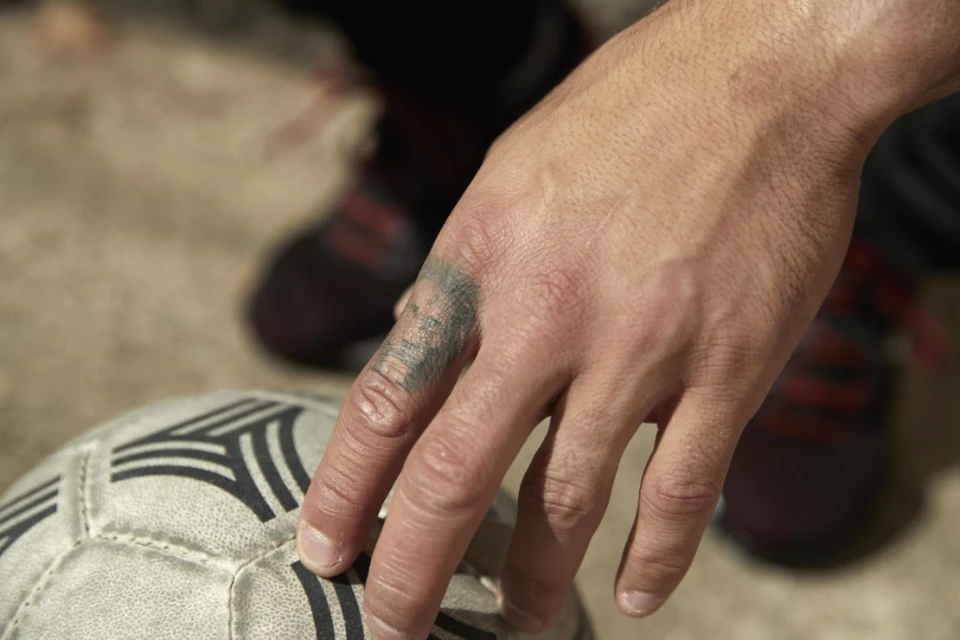 Close-up of a hand with a tattoo resting on a soccer ball, showcasing the textures of the skin, tattoo, and ball.