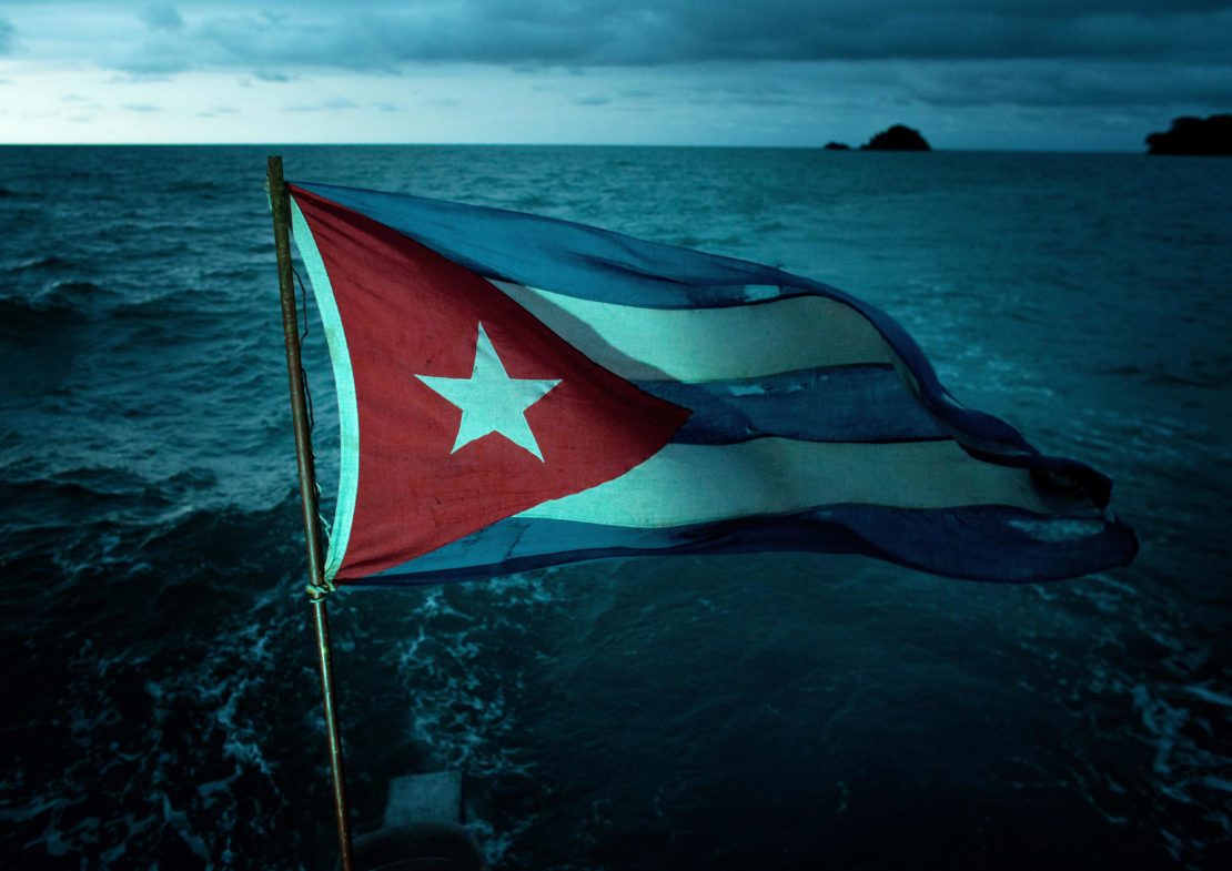 Waving Cuban flag with a single white star against blue ocean backdrop under an overcast sky, capturing a national symbol at sea.