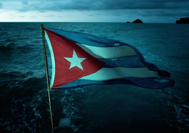 Waving Cuban flag with a single white star against blue ocean backdrop under an overcast sky, capturing a national symbol at sea.