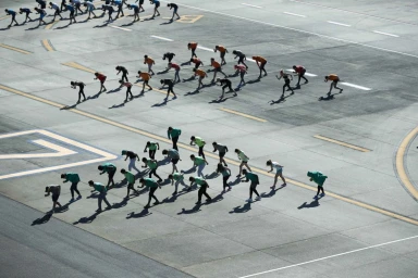 High angle photograph of a large group of runners assembled in formation on a wide asphalt tarmac.