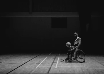 Black basketball player in a sports wheelchair holding a basketball on an indoor court shot by The Wade Brothers