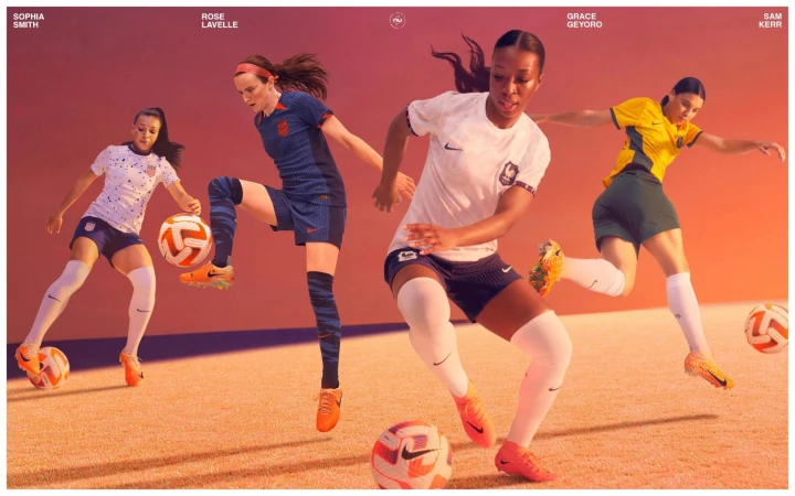 Four female soccer players in sports attire each kicking a soccer ball. The scene is set against a gradient background of orange and purple hues.
