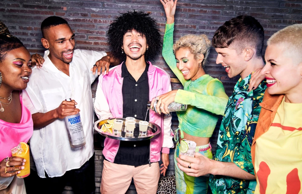 Diverse group of friends celebrates with cocktails and drinks in a bar setting, enjoying each other's company and vibrant atmosphere.