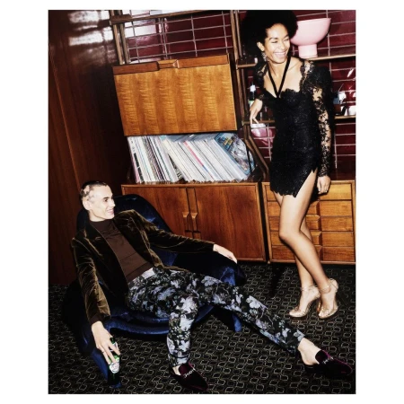 Stylish indoor shot of a woman in a short black dress and a man in a velvet blazer, with a mid-century cabinet and bar accessories.