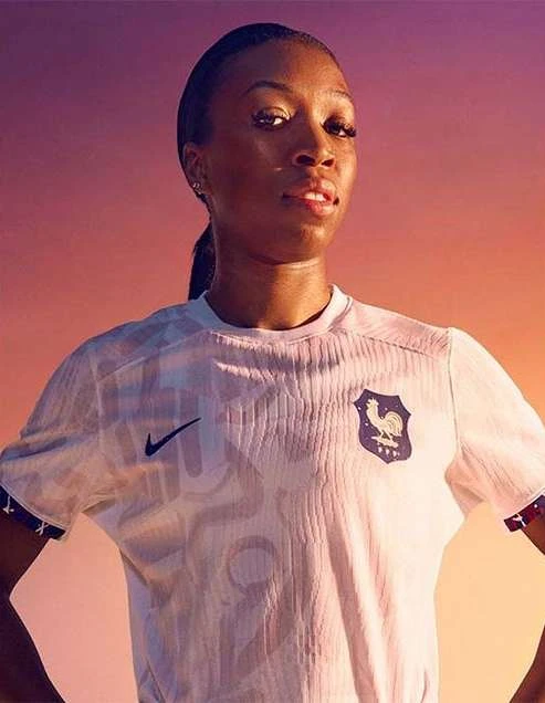 Portrait of a Black female athlete wearing a white soccer jersey with the French national team emblem against a gradient background.