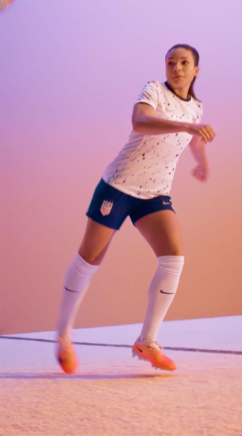 Female soccer player in US national team uniform in action, captured in a vibrant, dynamic studio setting. Focus on athletic performance.