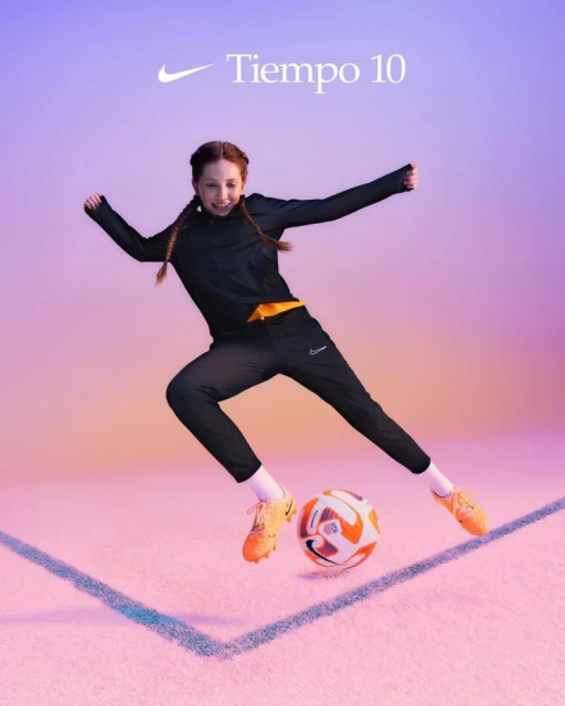 A young girl in sportswear mid-jump with a soccer ball on a field, showcasing athletic skill and fitness, set against a gradient background.